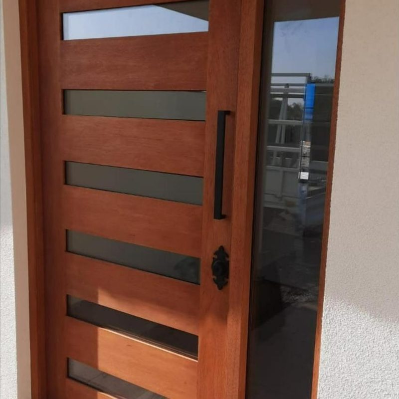 Puerta de madera con franjas de vidrio y paño lateral de cristal